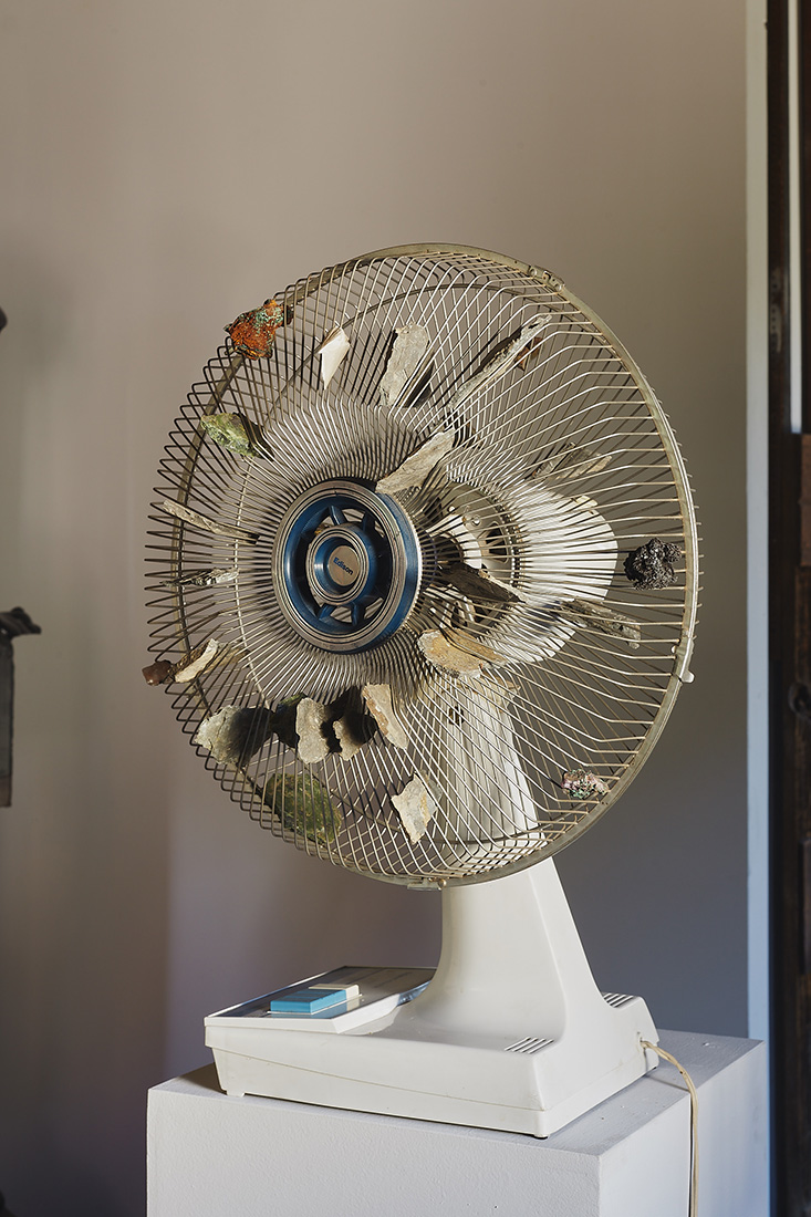 Rock-fan - A sculpture by Brian Dario, featuring a short standing fan with flat rocks attatched to its cage